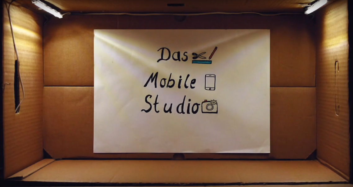Cover-mobile studio Einblick in das Mobile Studio - ein Pappkarton mit Leuchtstreifen. An der Rückwand ist ein Zettel angebracht mit der Aufschrift: